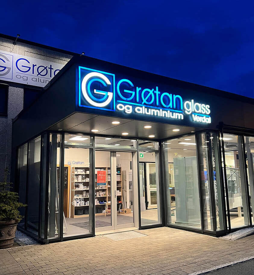 Fasadeskilt med lys for Grøtan Glass og Aluminium på kveld.